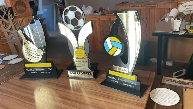 Troféus com raquete, bola de futebol e bola de vôlei sobre bancada