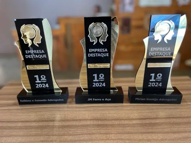 Três troféus pretos, transparentes e dourados com inscrição Empresa Destaque