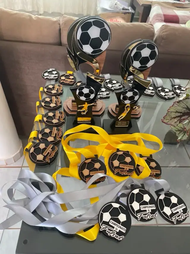 Conjunto de troféus com bolas de futebol e medalhas com fitas amarelas e brancas