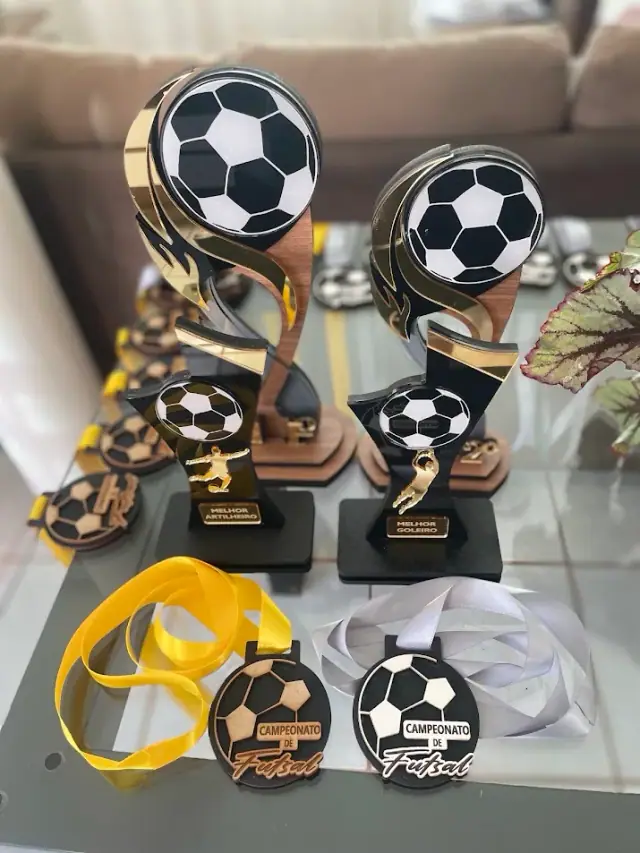 Troféus pretos e dourados com bolas de futebol ao lado de medalhas com fitas
